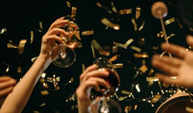 people raising their glasses as gold confetti falls around them