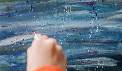 a person uses their hand paint fine lines on a painted canvas