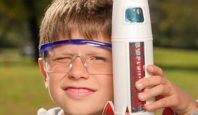 a young boy wearing goggles, holding a model rocket ship