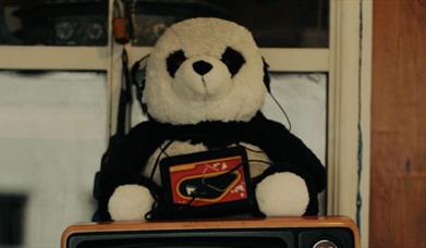 a stuffed panda toy is listening to a toy tape player with headphones