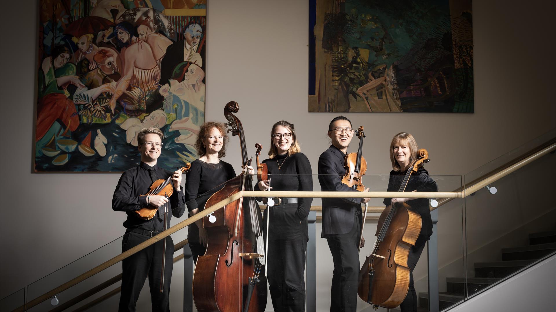 A group of orchestral musicians holding their instruments and standing in a line on a staircase.