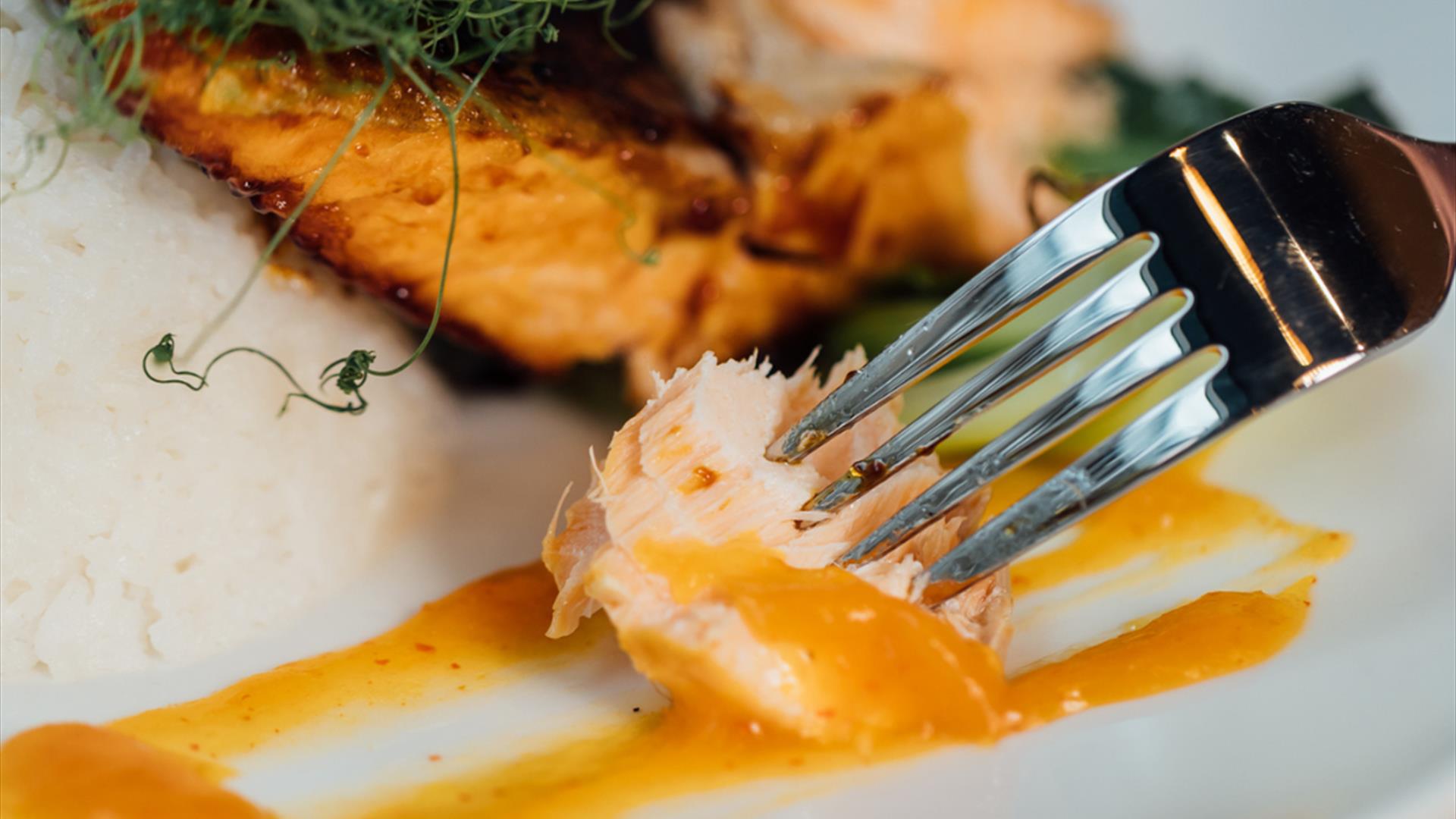 a plate of cooked fish, with a morsel on a fork covered in sauce