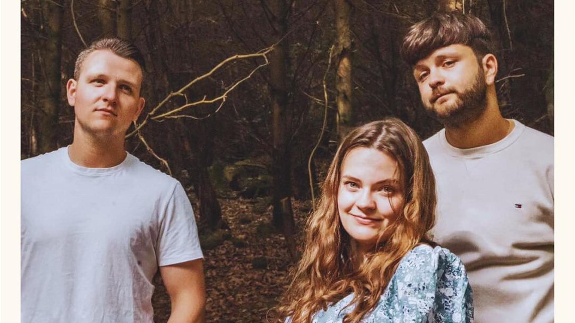 Image of 3 people standing outdoors looking at the camera, there is a forest in the background