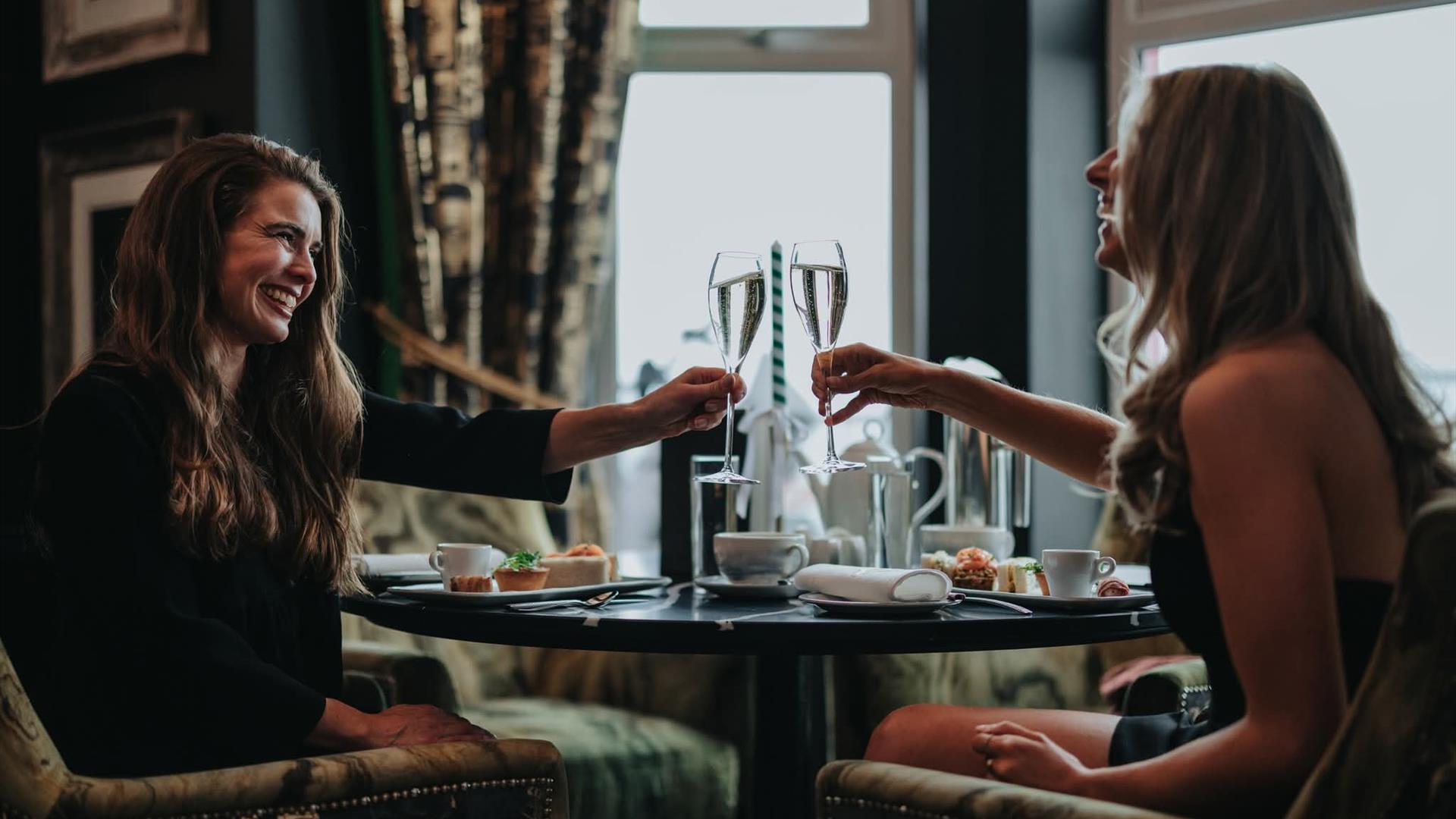 two women clink their prosecco glasses together over a table at Elephant Rock Hotel