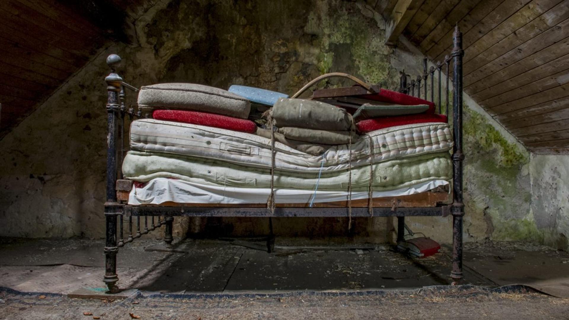 a bedframe with many mattresses stacked up on it in an empty attic