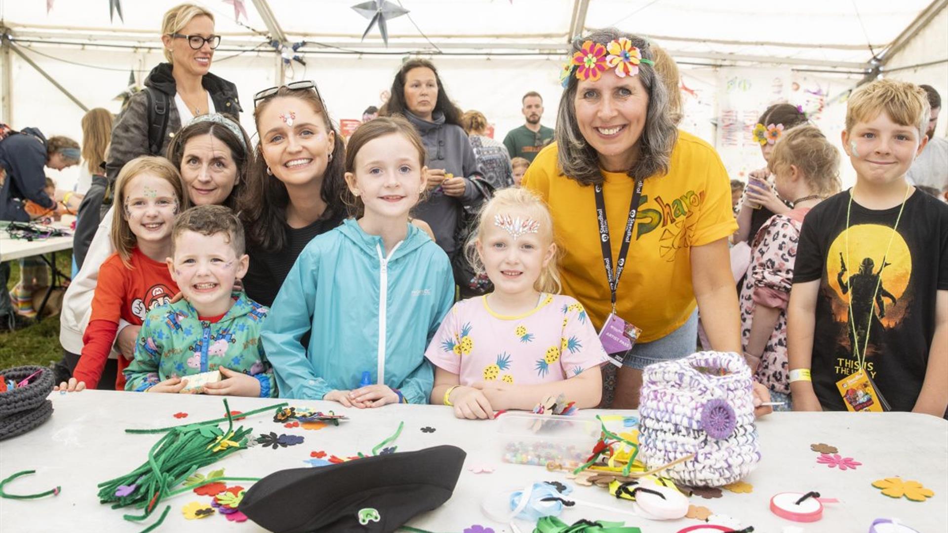 Children and adults  smiling in front of a table of colourful crafts and expressive pendants.