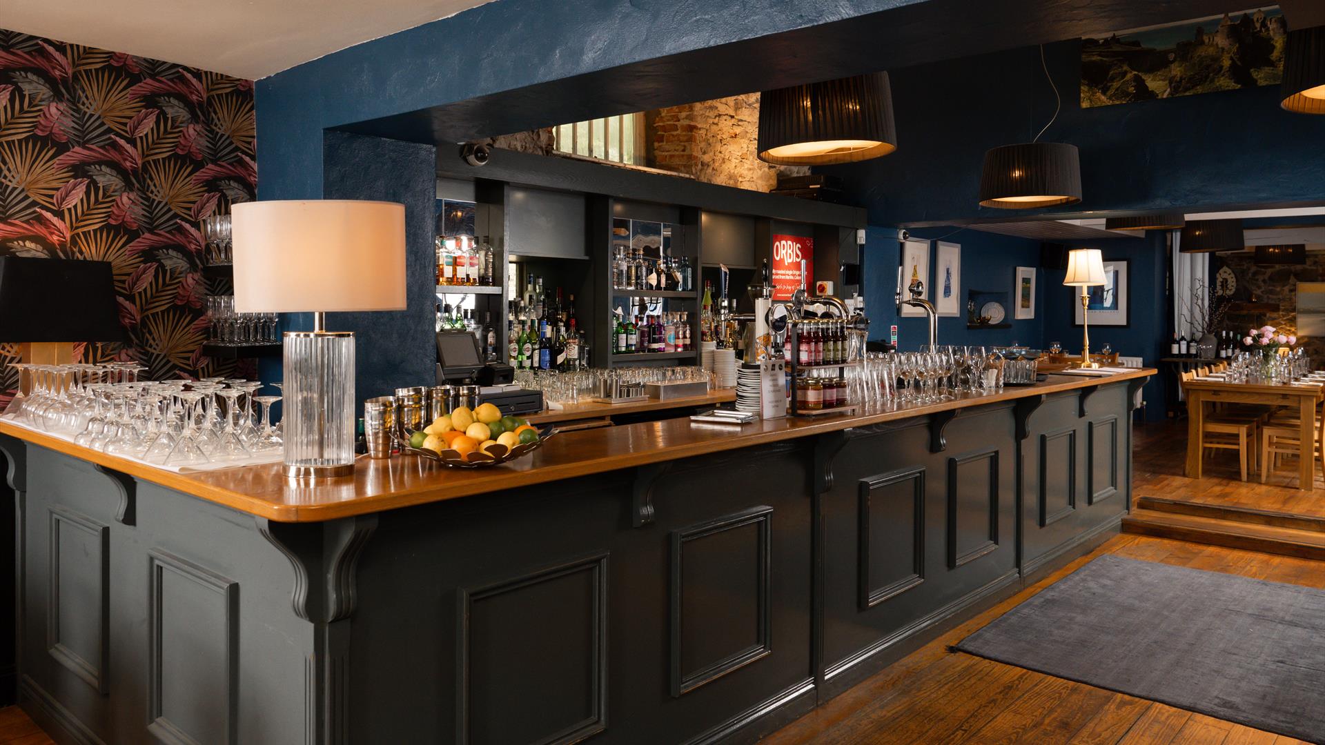 interior of Tartine at Distiller's Arms Restaurant, Bushmills, which features a large black panelled bar with a brown wooden bar top which holds sever