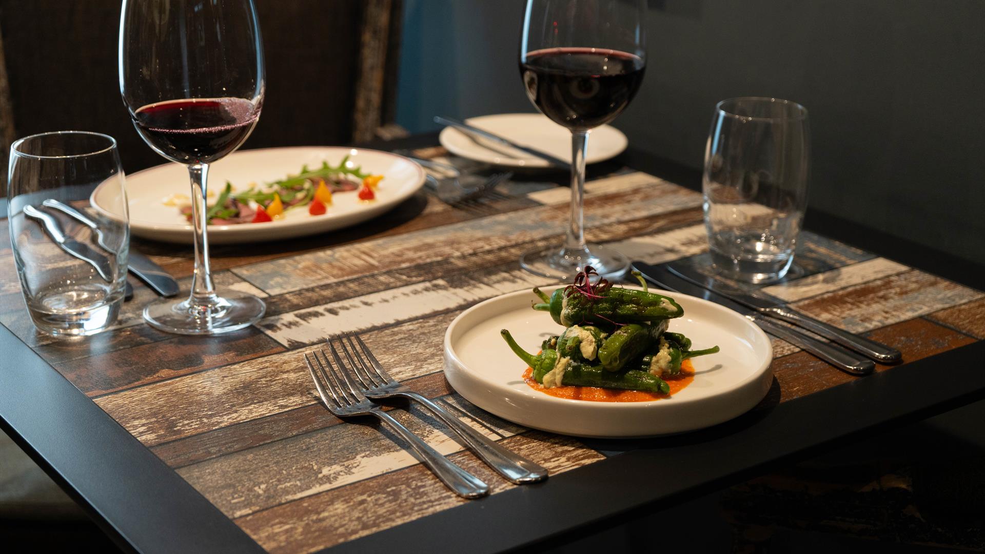 dishes of food and red wine sit on a wooden dining table