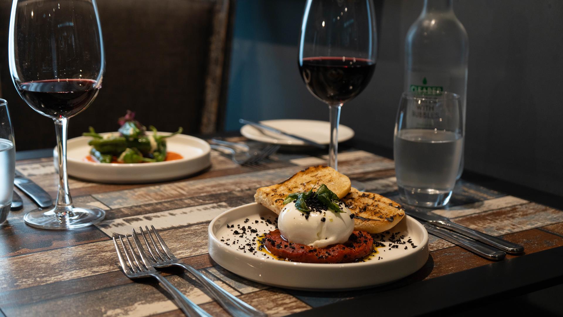 dishes of food and wine glasses sit on top of a wooden table