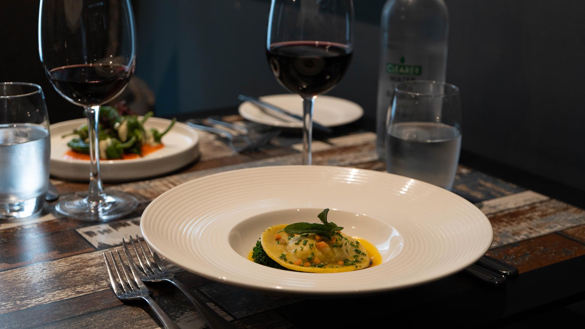 Italian food in dishes and red wine sit on a table in a restaurant