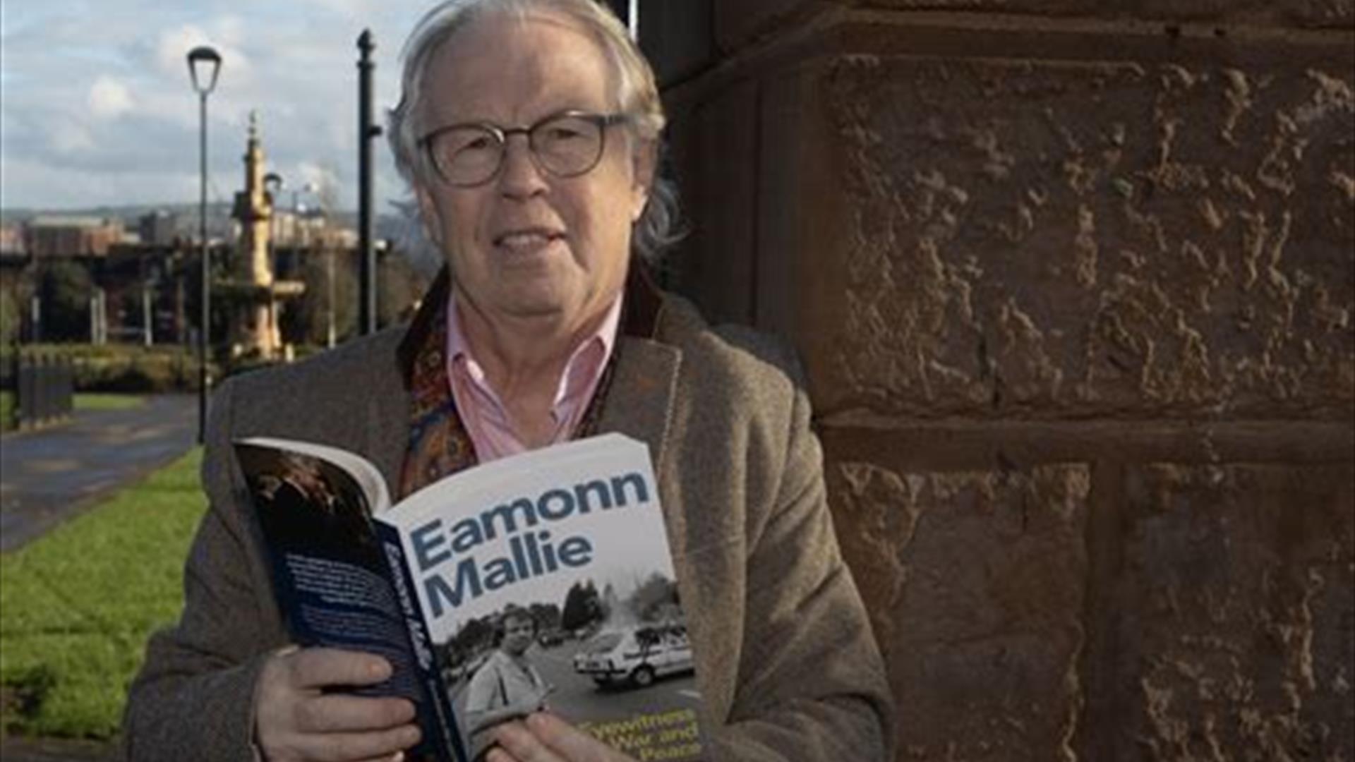 Eamonn Mallie stands holding his book