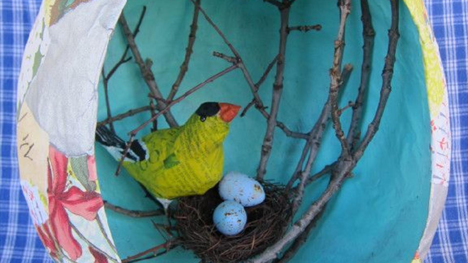 a paper-mache easter egg with a crafted bird and nest inside