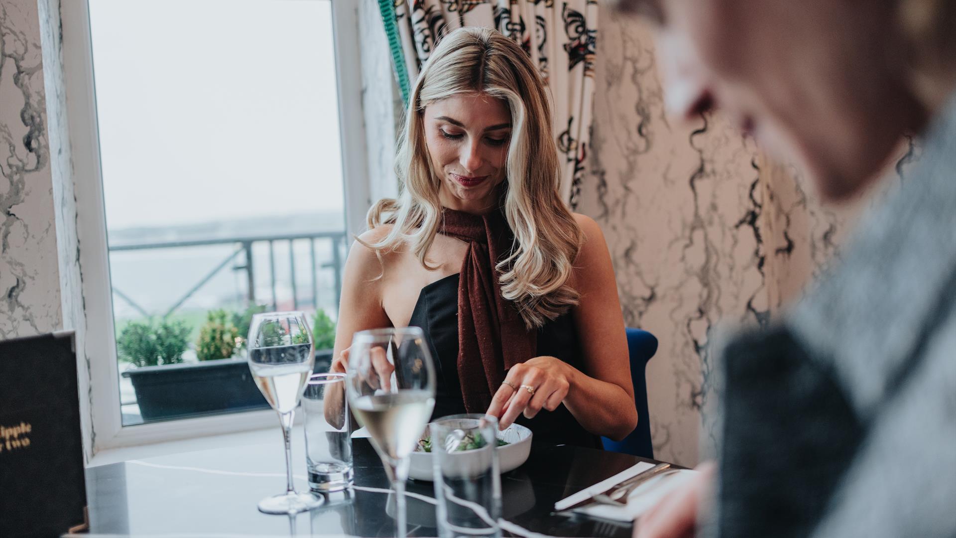 a man and woman sit at a table, eating food and drinking wine with a view from the elephant rock hotel