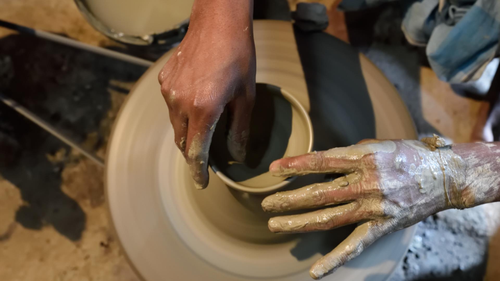 a person working on a pottery wheel, their hands covered in clay