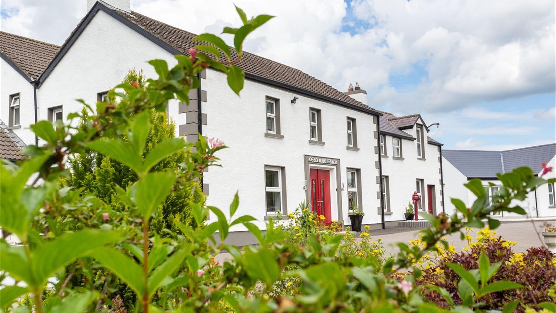 Exterior view of Willow House, a white Edwardian manor with a red front door and lush green garden foreground.