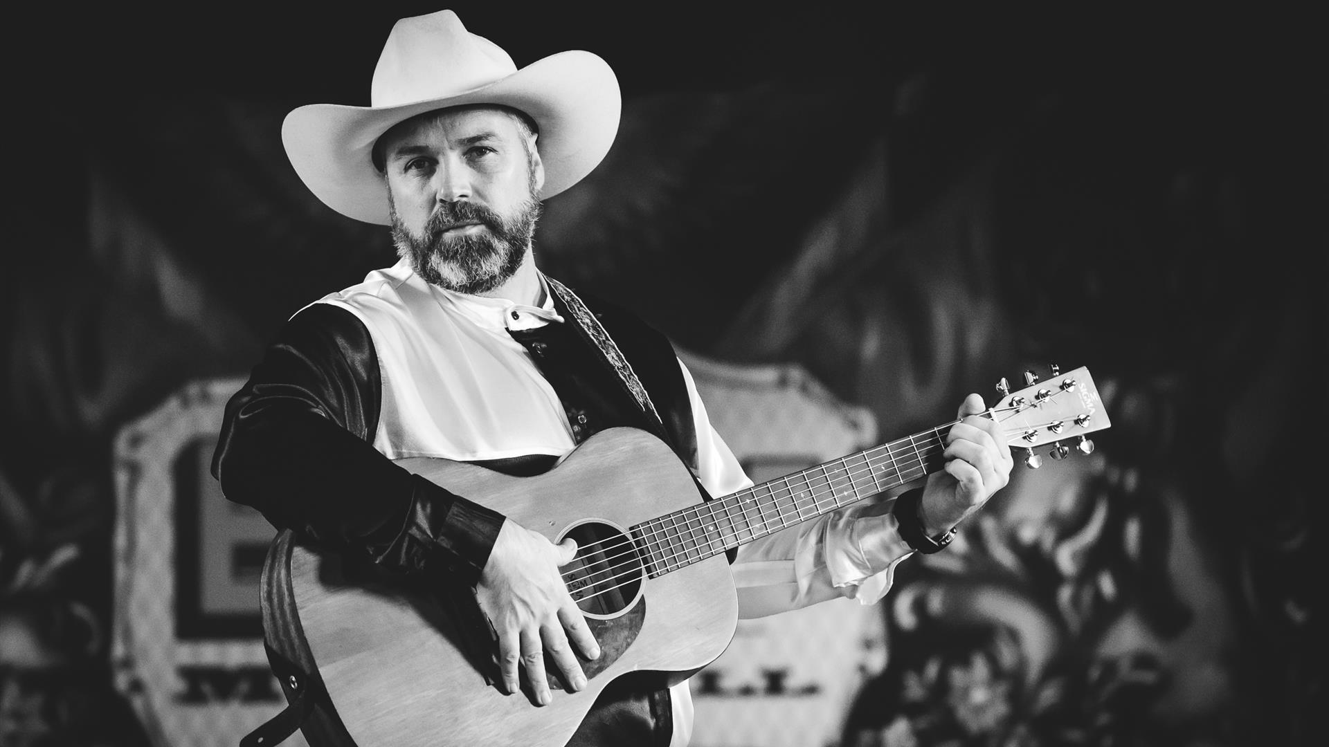 Black and white photograph o Stephen Butler with a guitar in a cowboy hat.