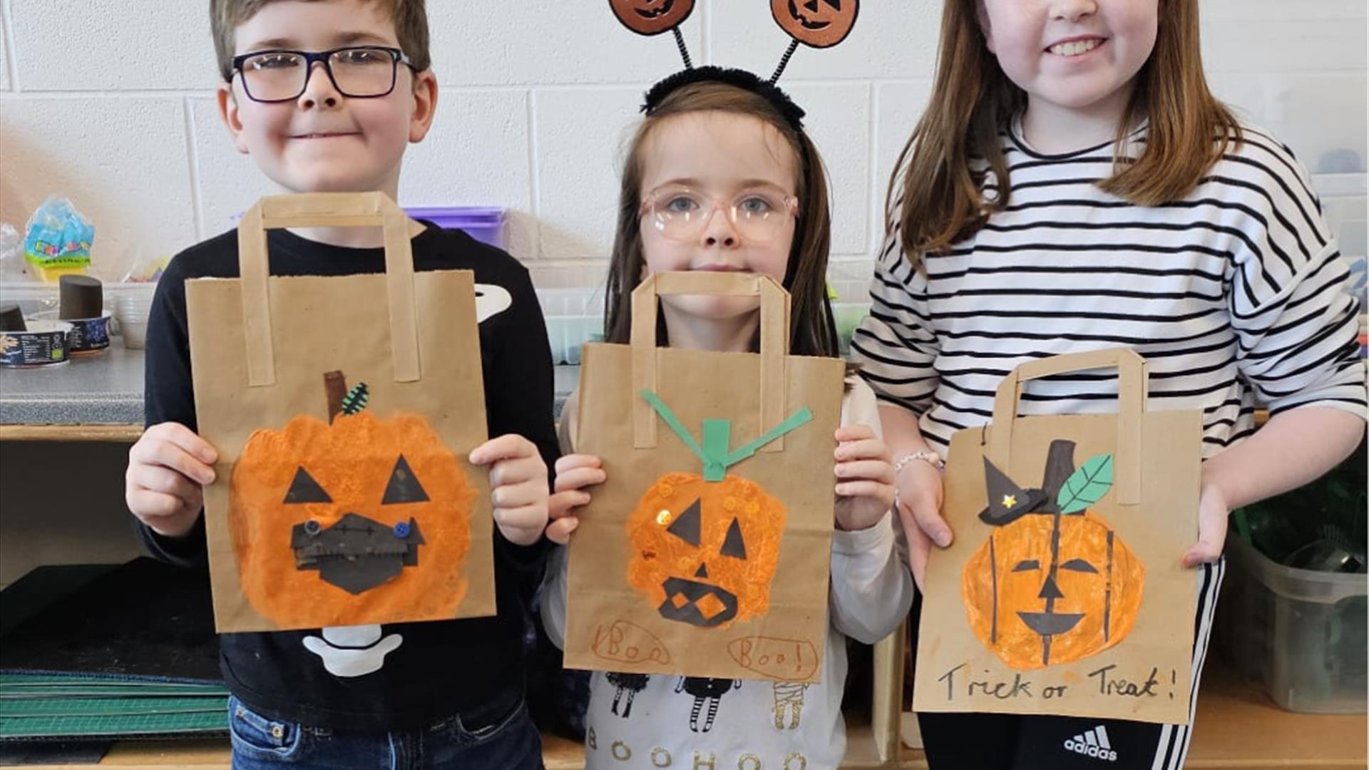 Imae of 3 children holding up their hand decorated pumpkin trick of treat bags.