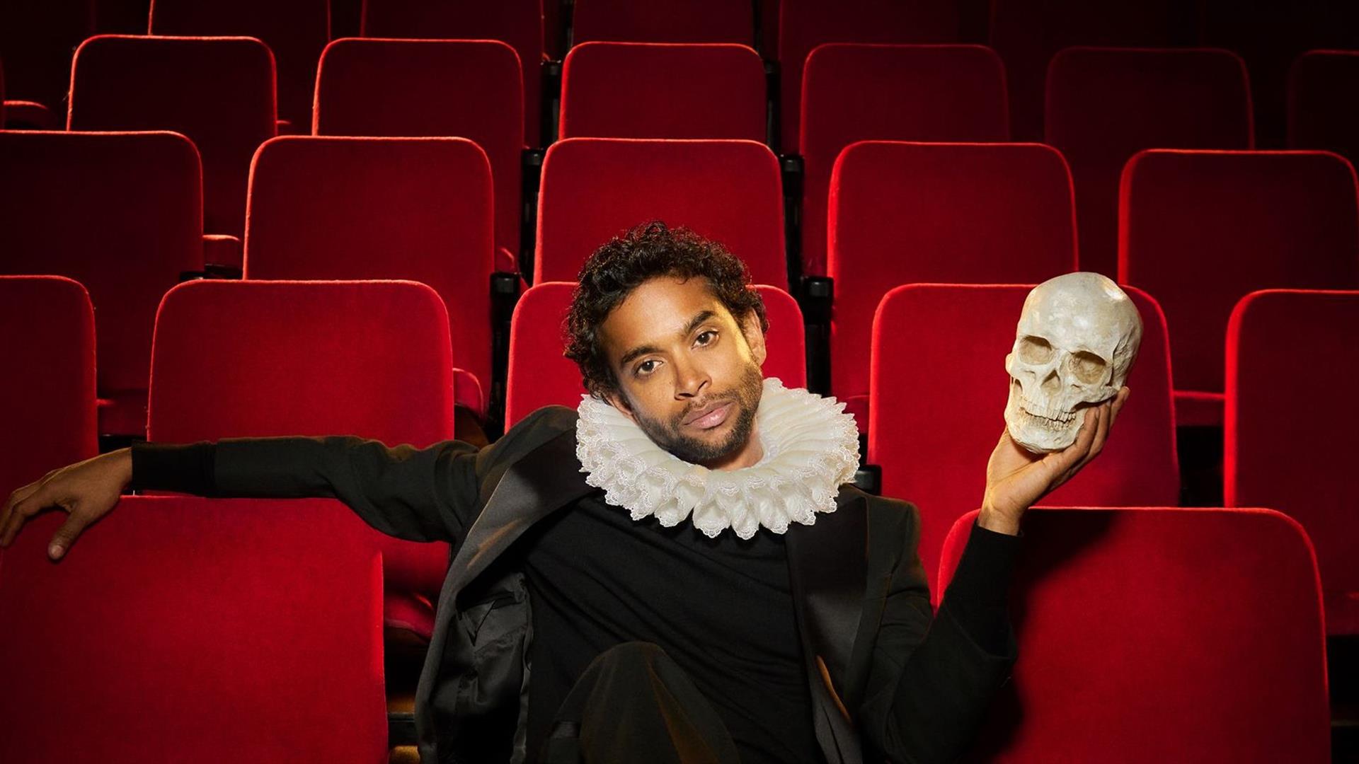 Hiran Abeysekera reclining across theatre seats holding a skull