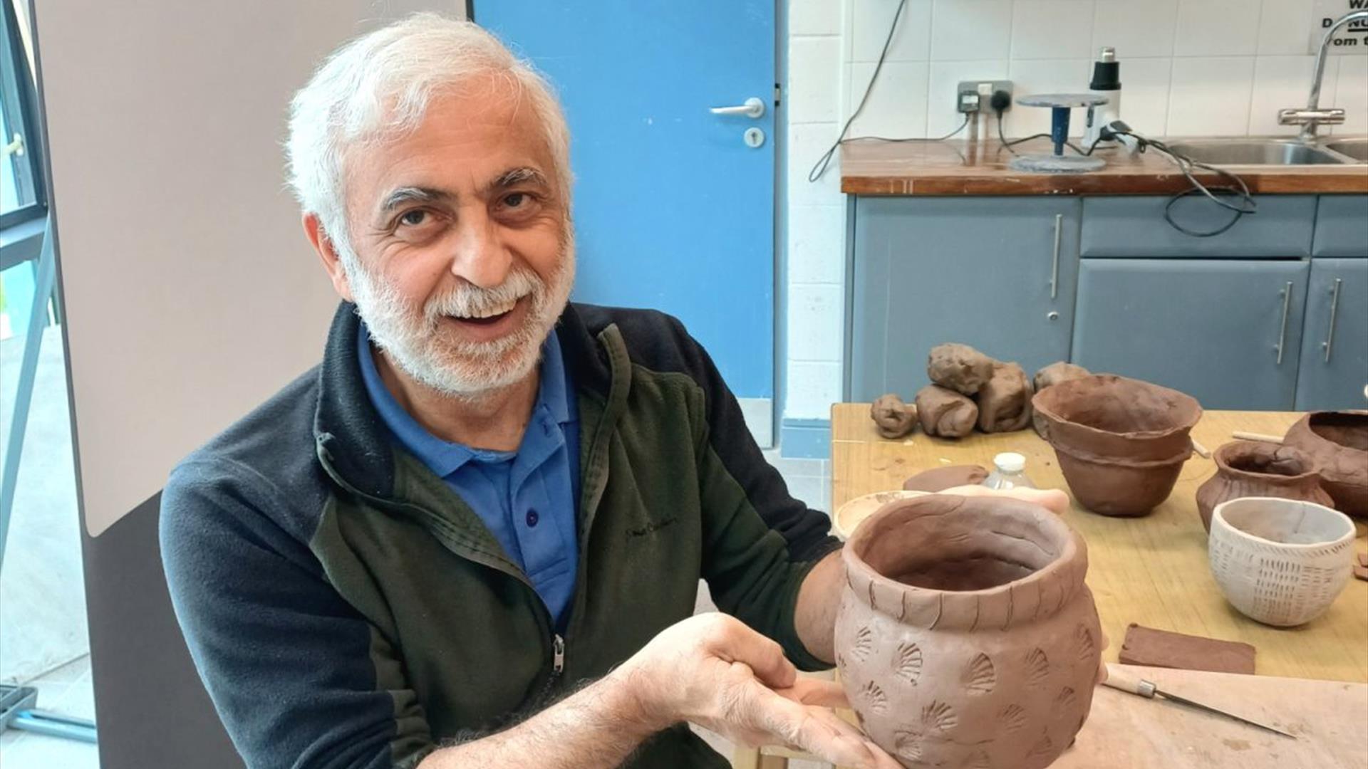 a man proudly presents a hand sculpted pot