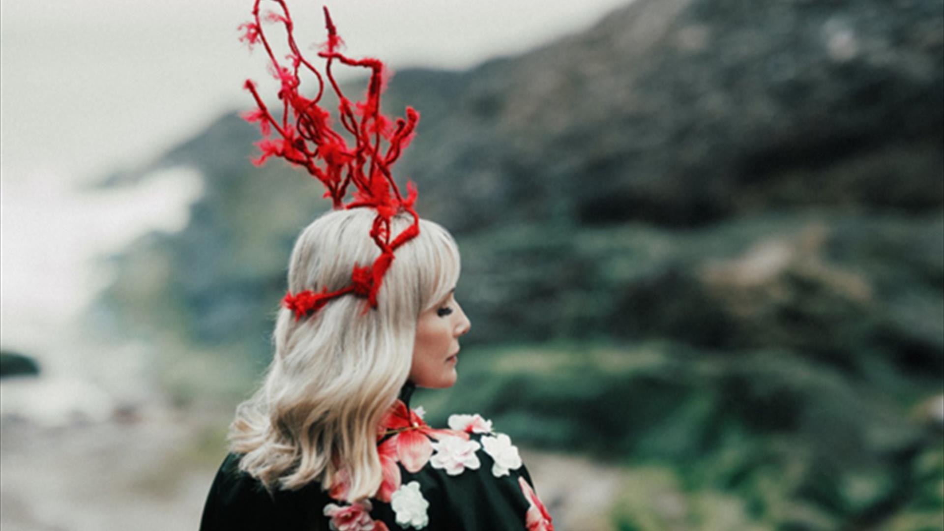 Image of a woman outdoors in a floral outfit with a red headdress on