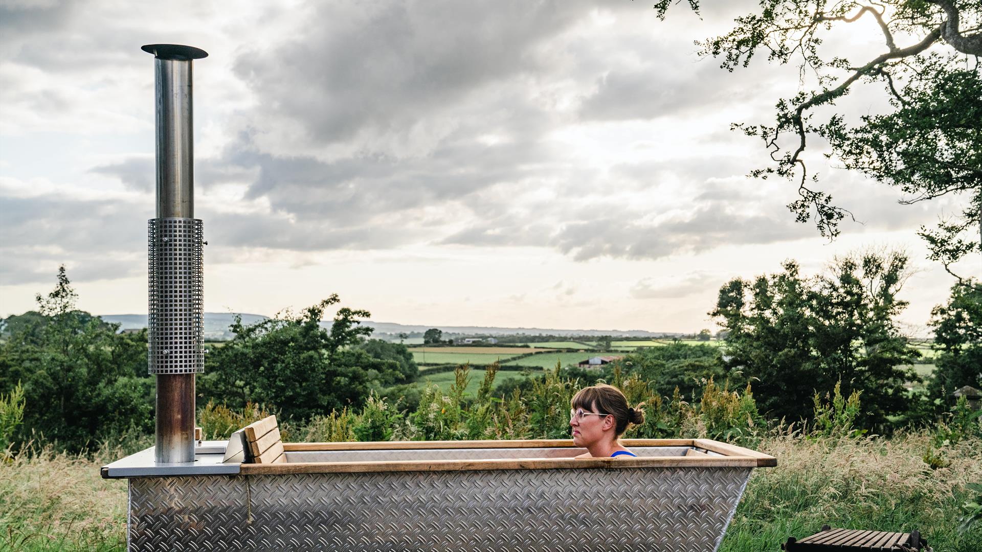 A lady reclines in the hot tub with views of the countryside in the backdrop