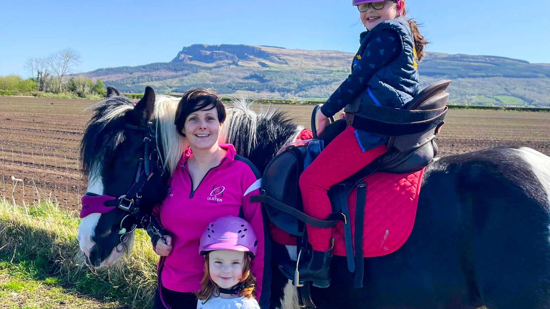 a woman and two children pose with a horse with Binevenagh Mountain in the background