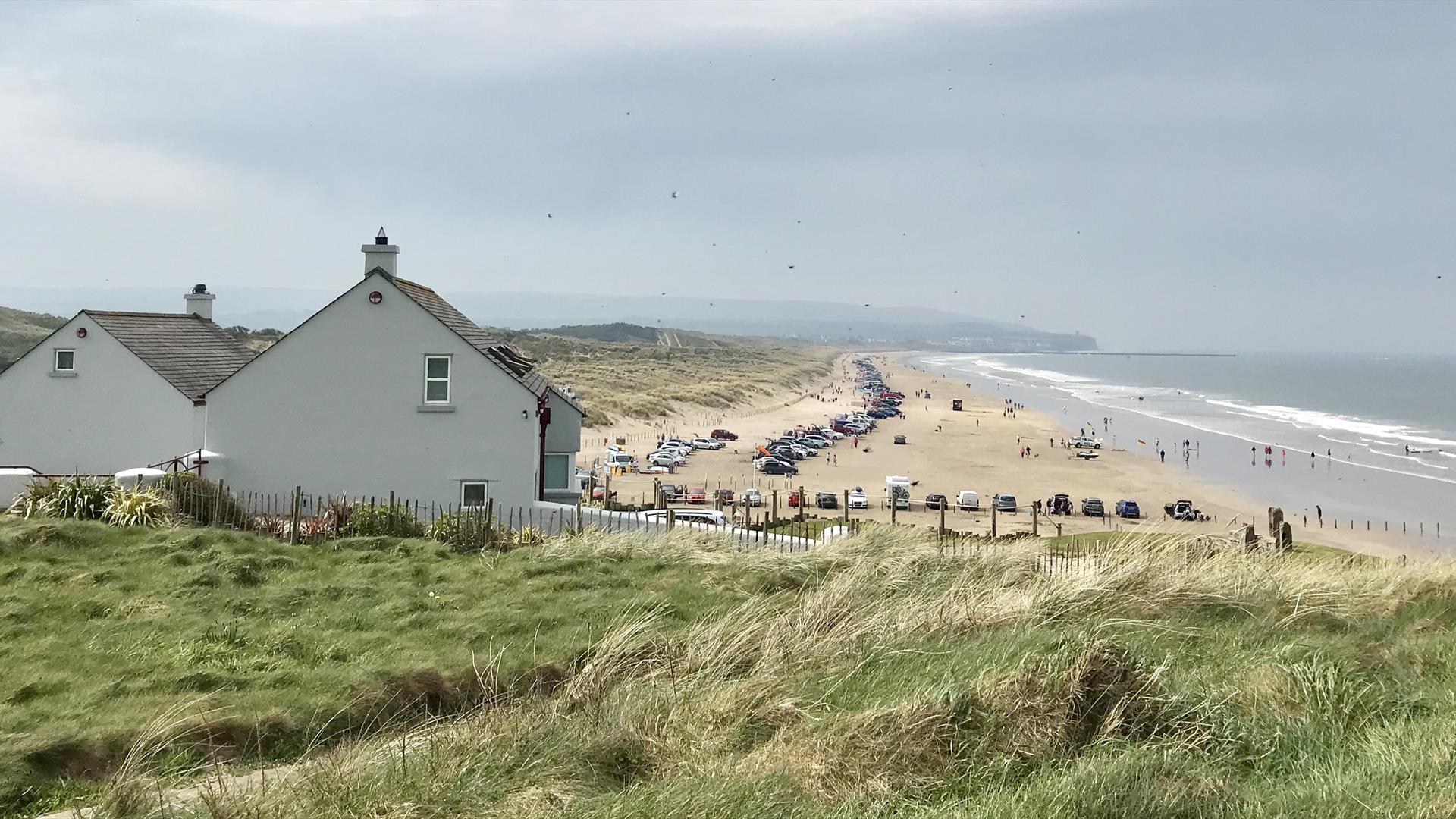 A view over Portstewart Strand in the busy summer season with cars parked all along the beach and families enjoying their day out.