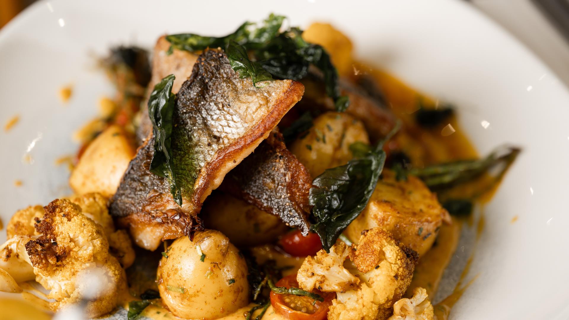 close up of a seafood dish on a plate; pieces of fish, cauliflower, spinach and potatoes are visible