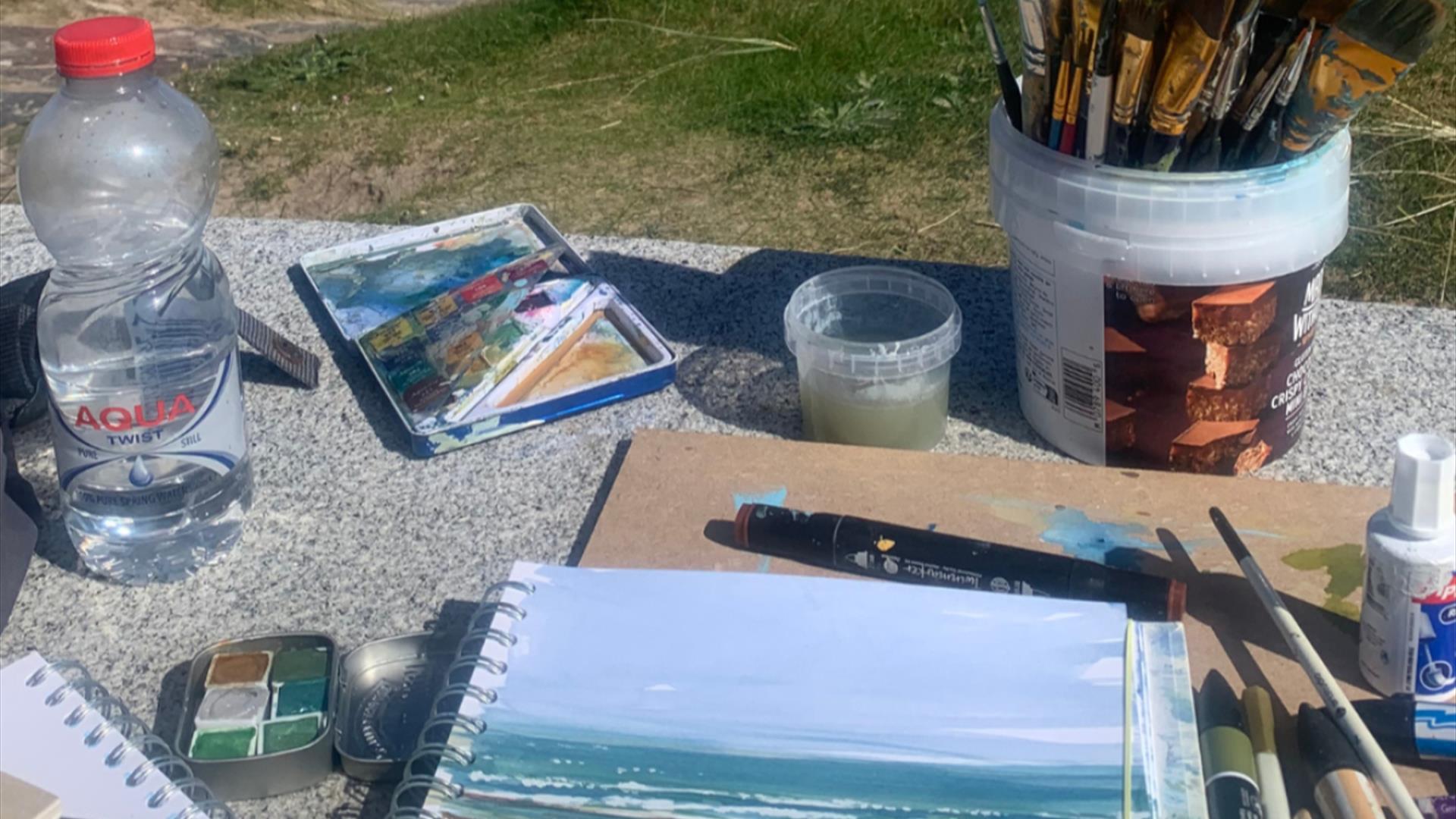 art supplies all gathered on an outdoor table with grass in the background