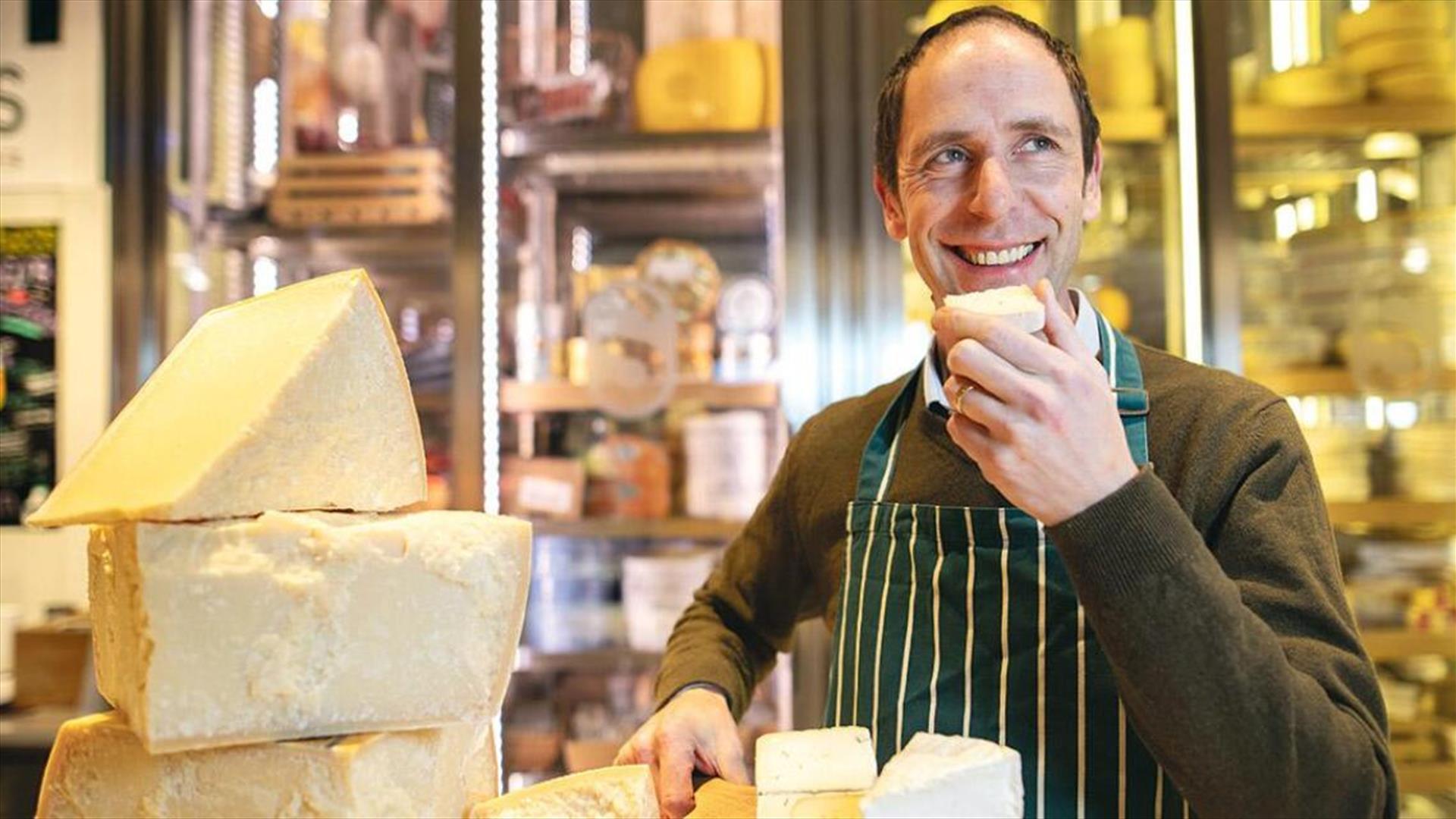 Kevin Sheridan in a striped apron, smiles while tasting cheese