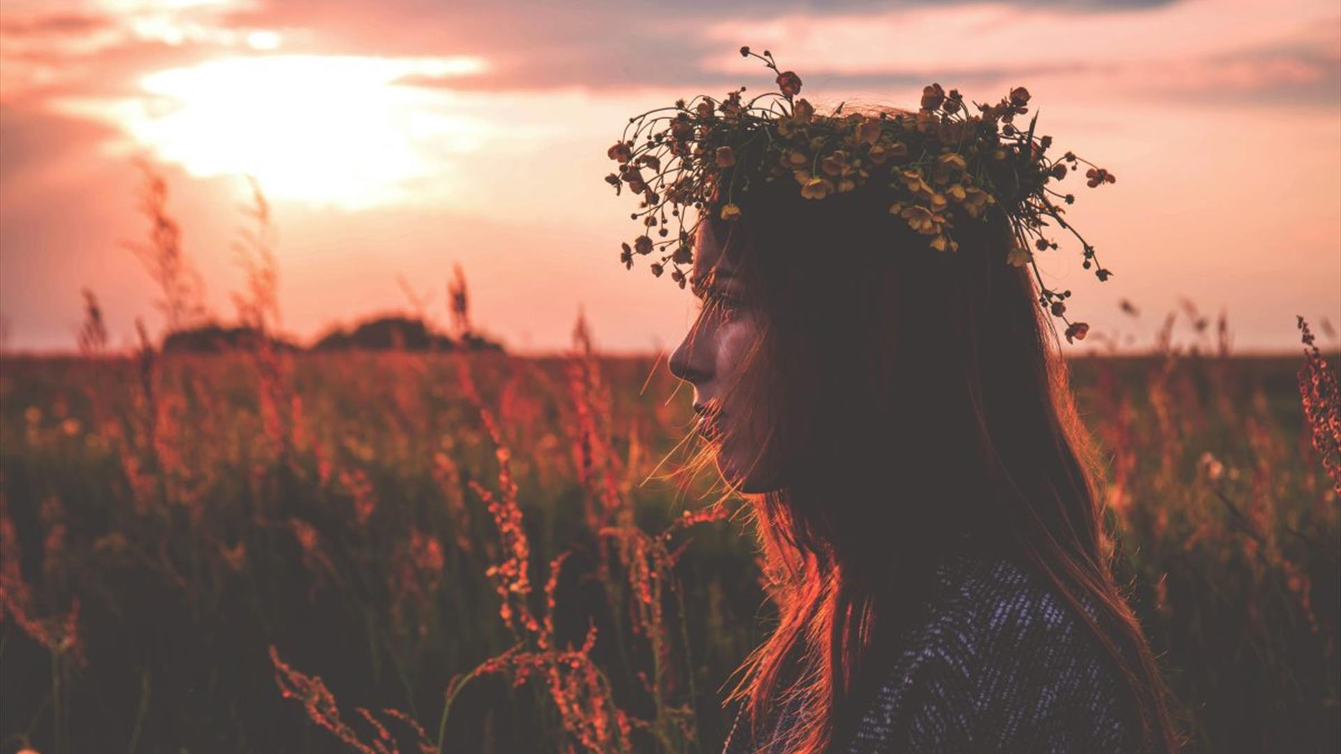 a woman with a floral crown standing against a summer sunset