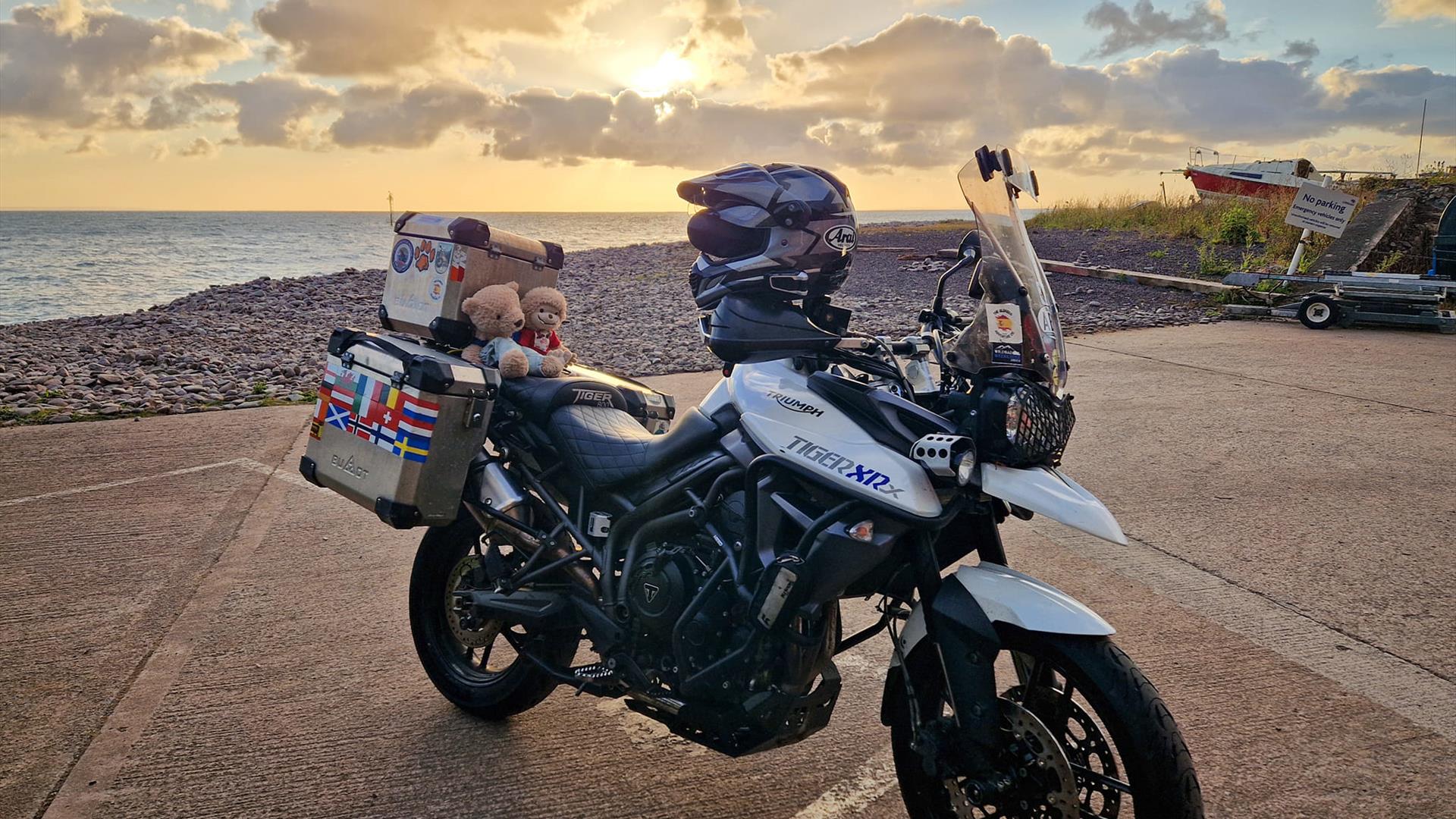 A motorbike on the beach at sunset, with a small bear riding pillion.