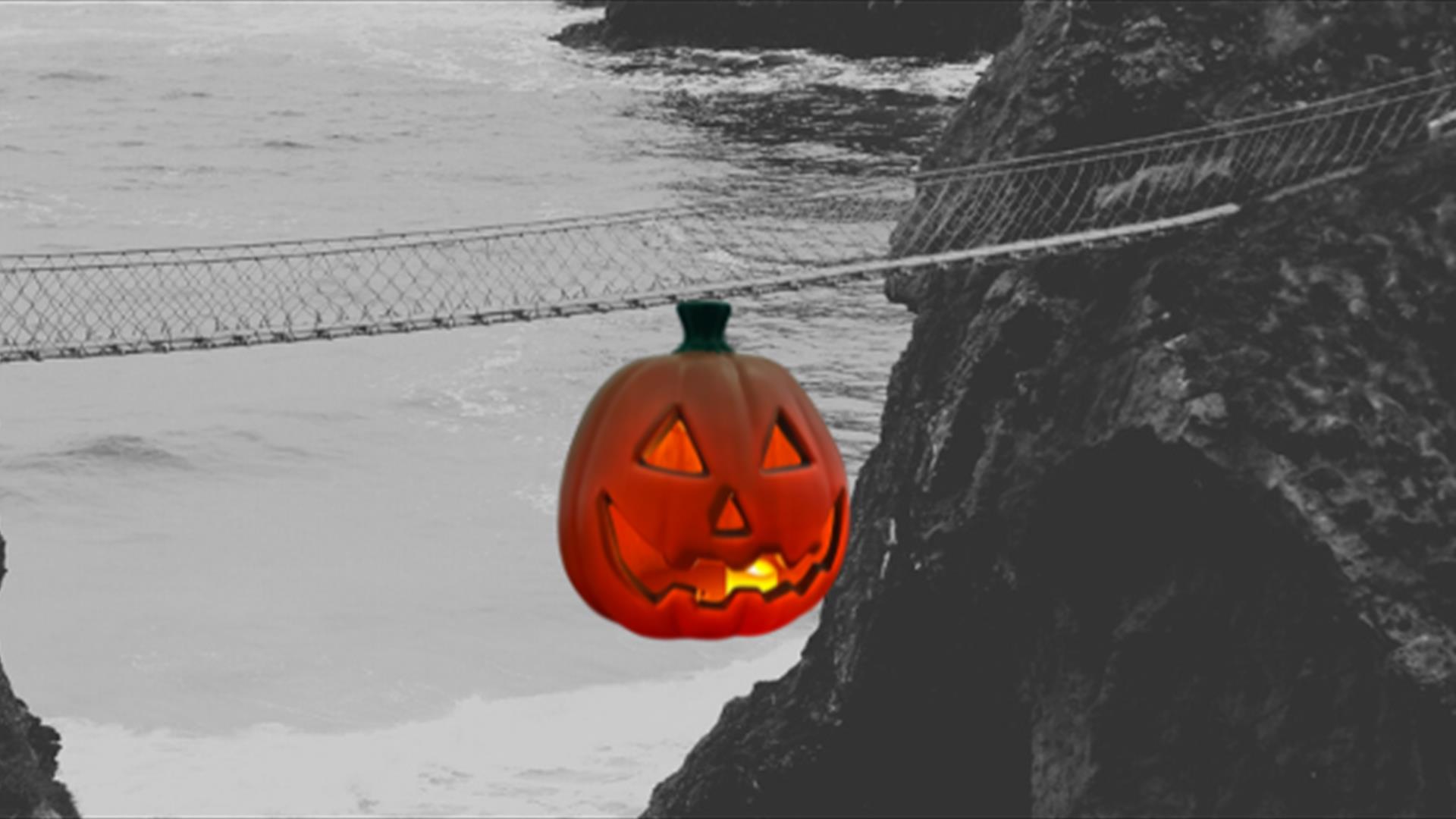 Black and White Picture of Carrick-a-Rede Rope Bridge  for Halloween, with a pumpkin graphic hanging from the bridge