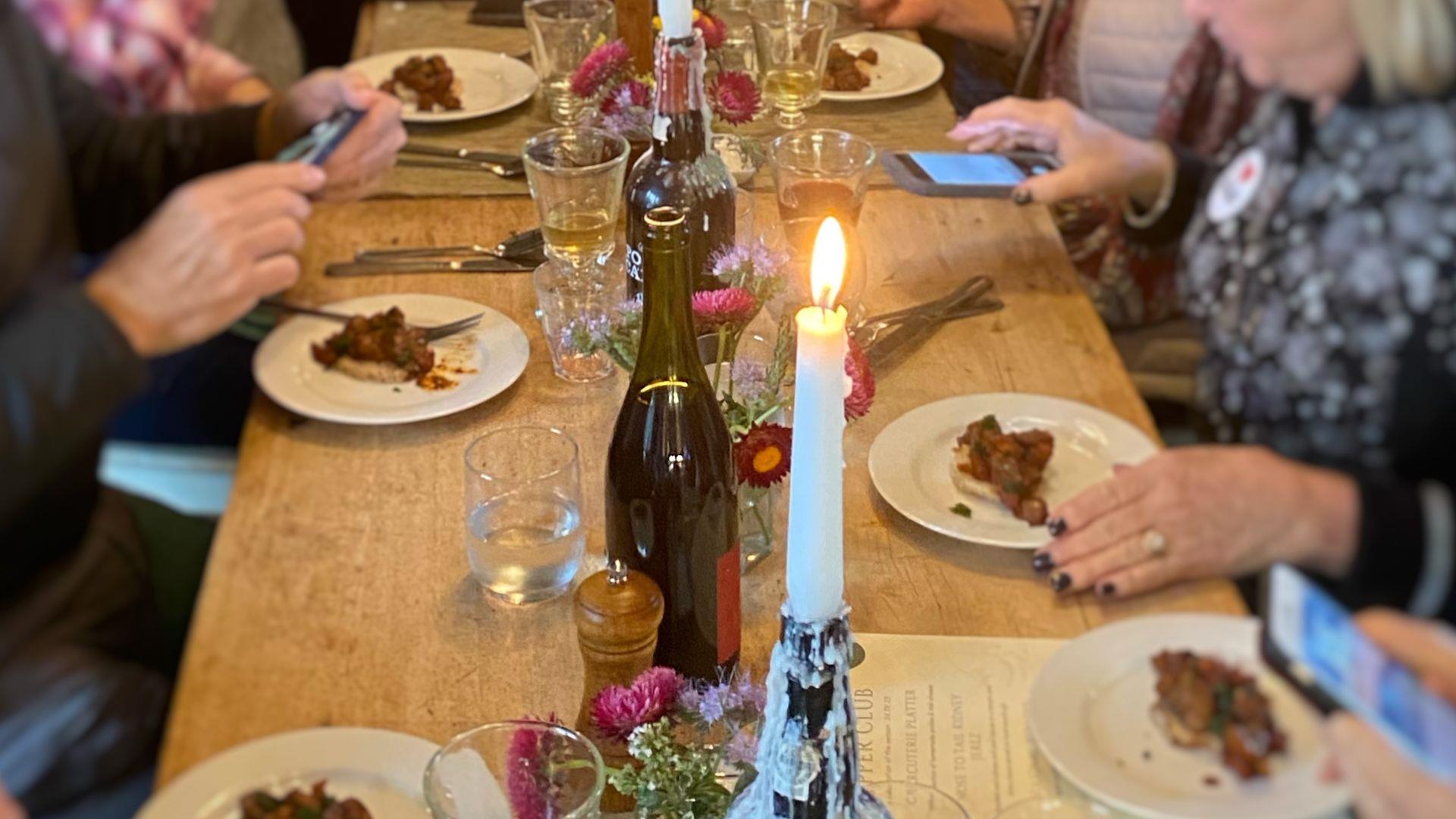 people are eating at a large wooden table by candlelight