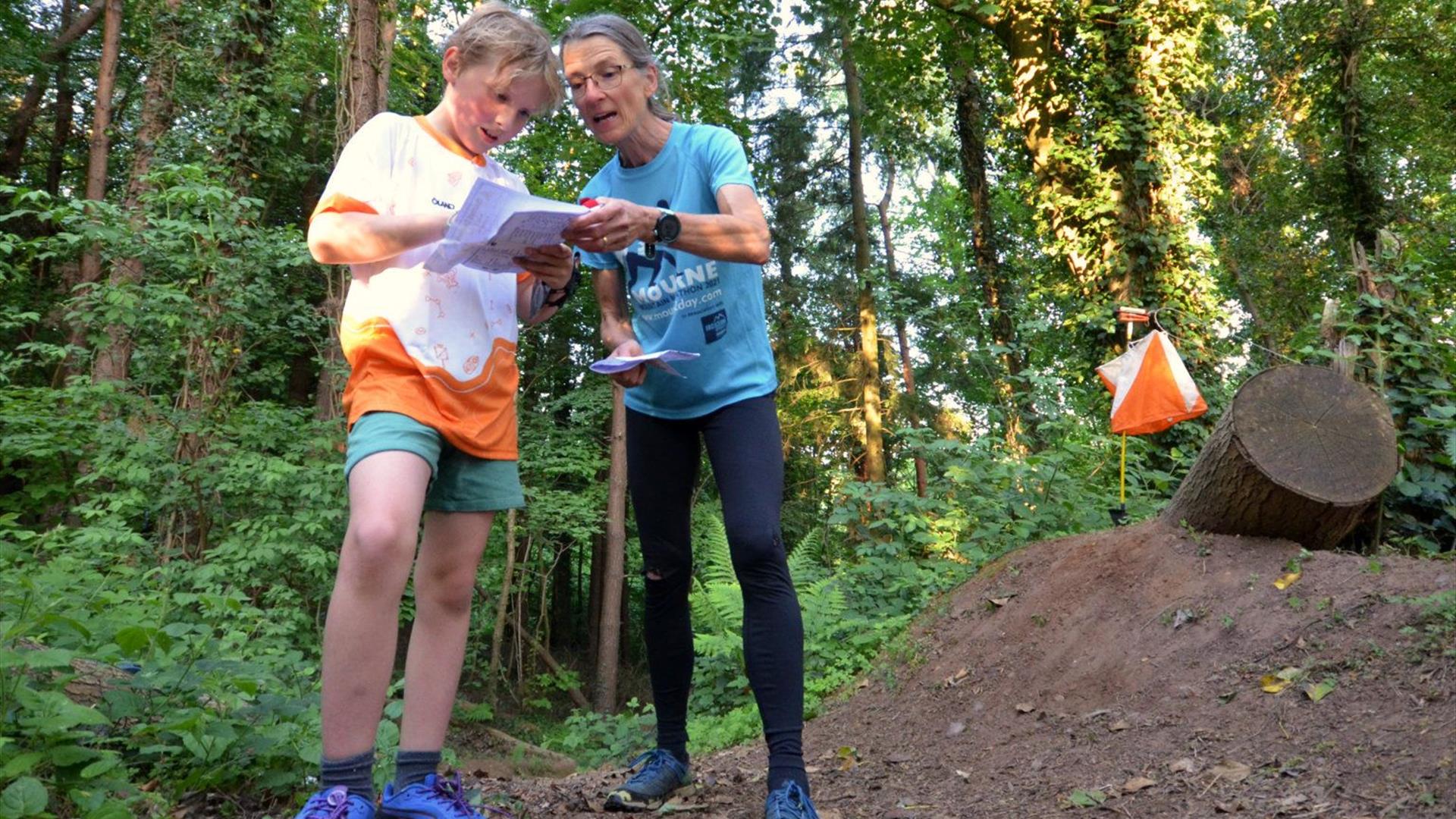 A woman and a young boy in the woods, reading a map together.