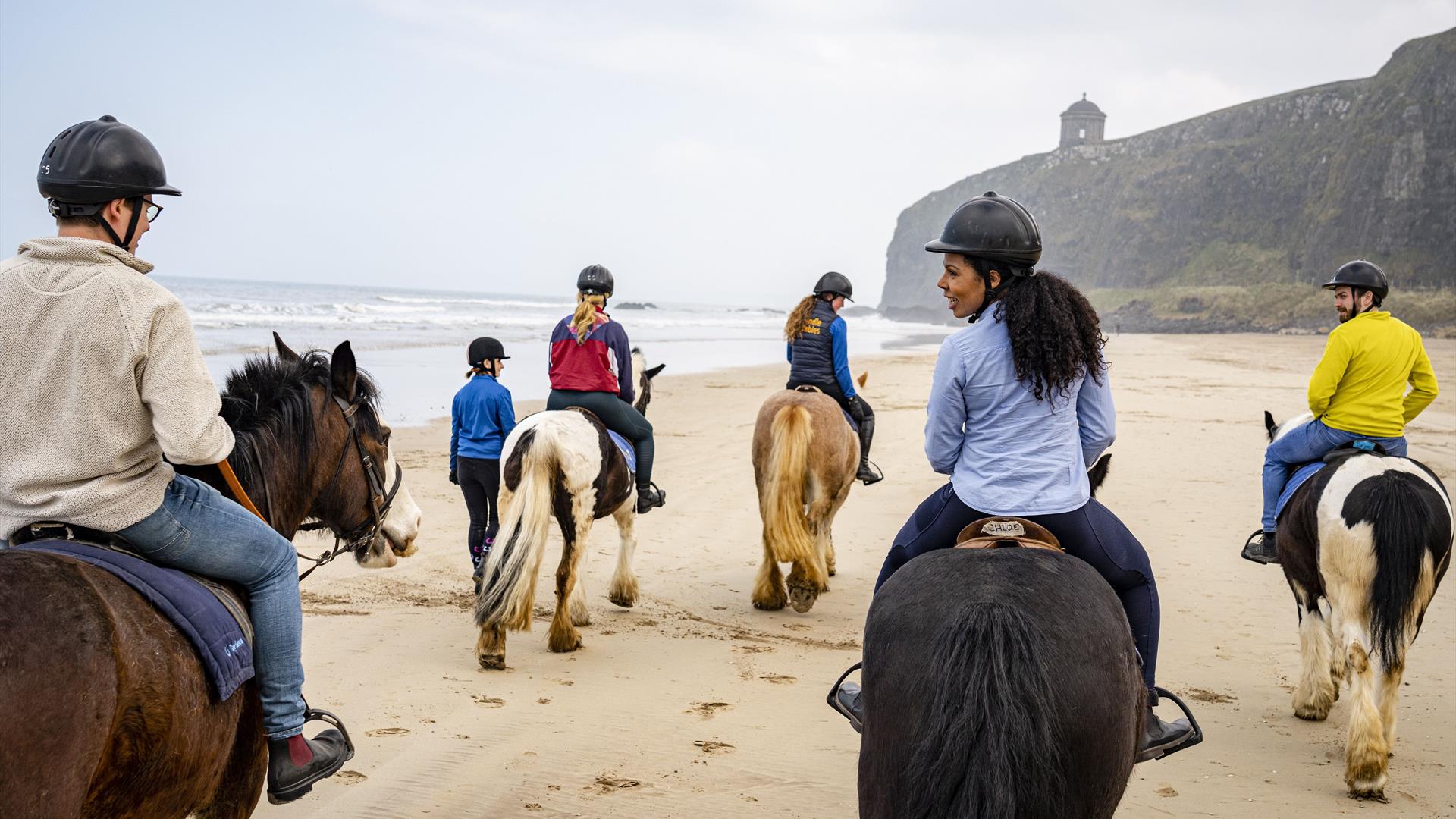 a group of people on horseback on Downhill Beach with Mussenden Temple visible in the distance