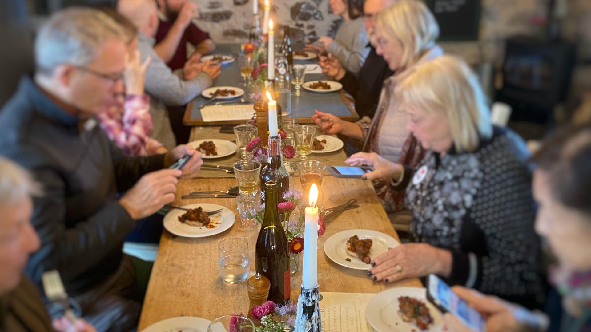 People sitting either side of a long wooden table decorated with candles and wine bottles.