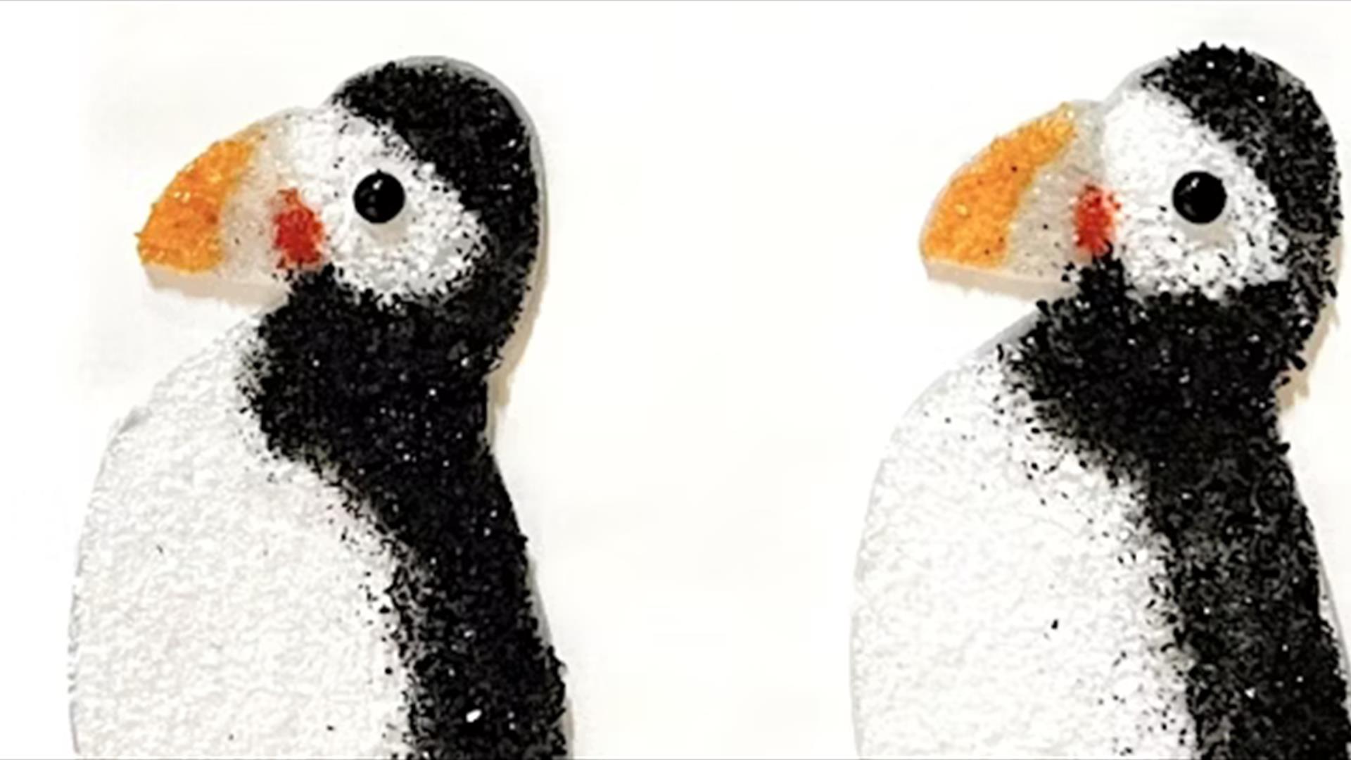 Two glass puffins facing left. They are flat against a white background.
