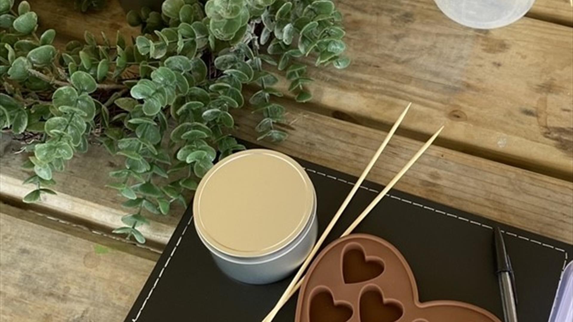 a wax melt mould sits on a wooden table, with a candle burning and other tools for making candles