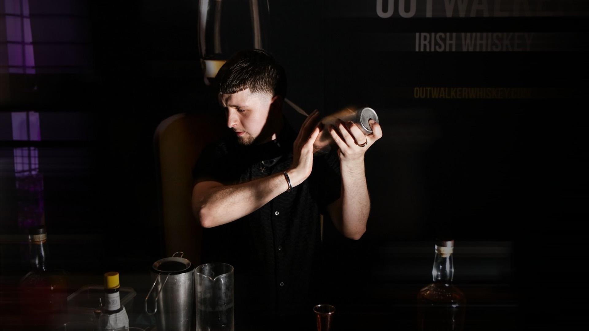 Man holding a cocktail shaker in a dimly lit bar setting