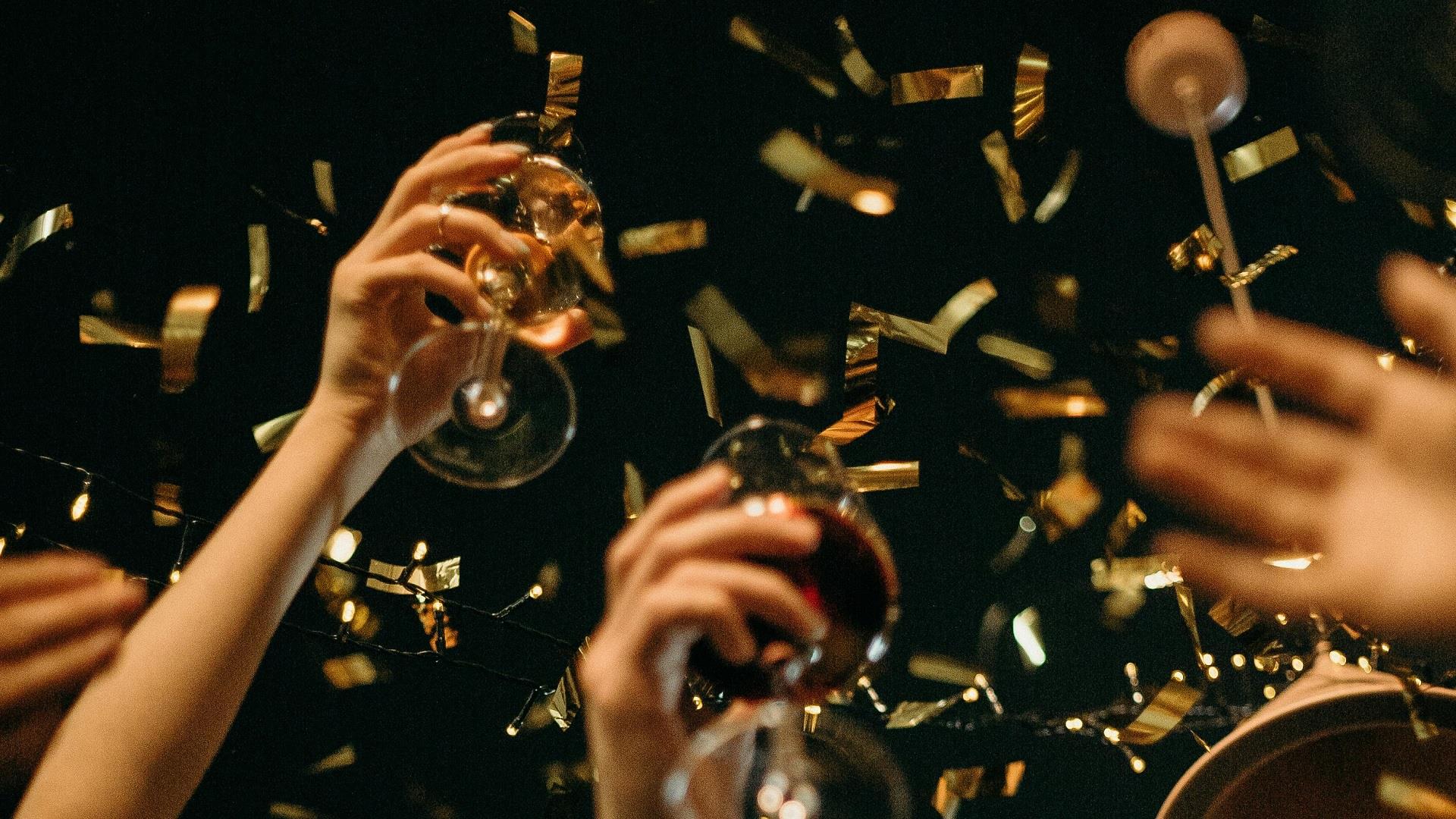 people raising their glasses as gold confetti falls around them