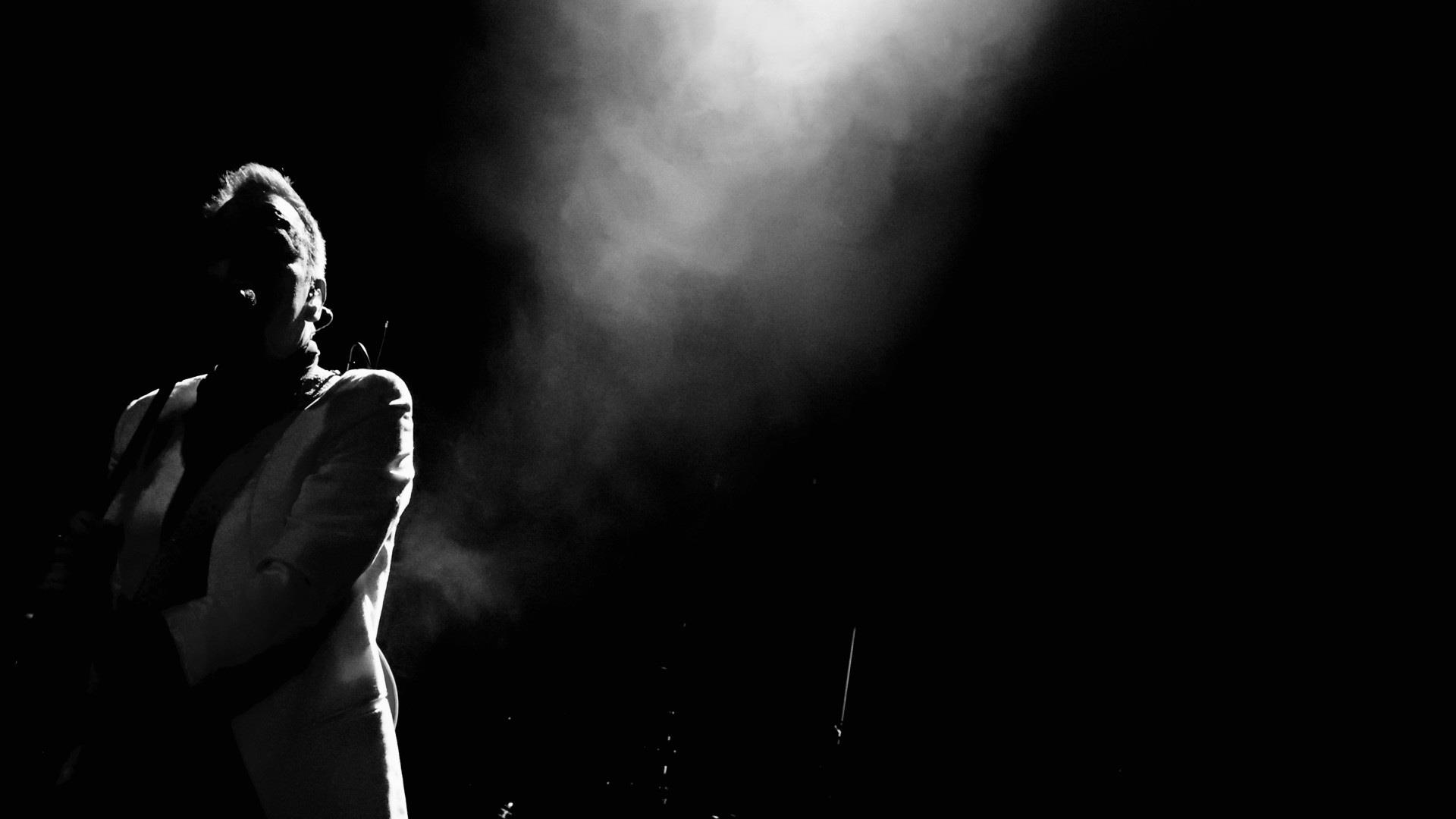 black and white image of male figure in shadows with a spotlight shining down on him.
