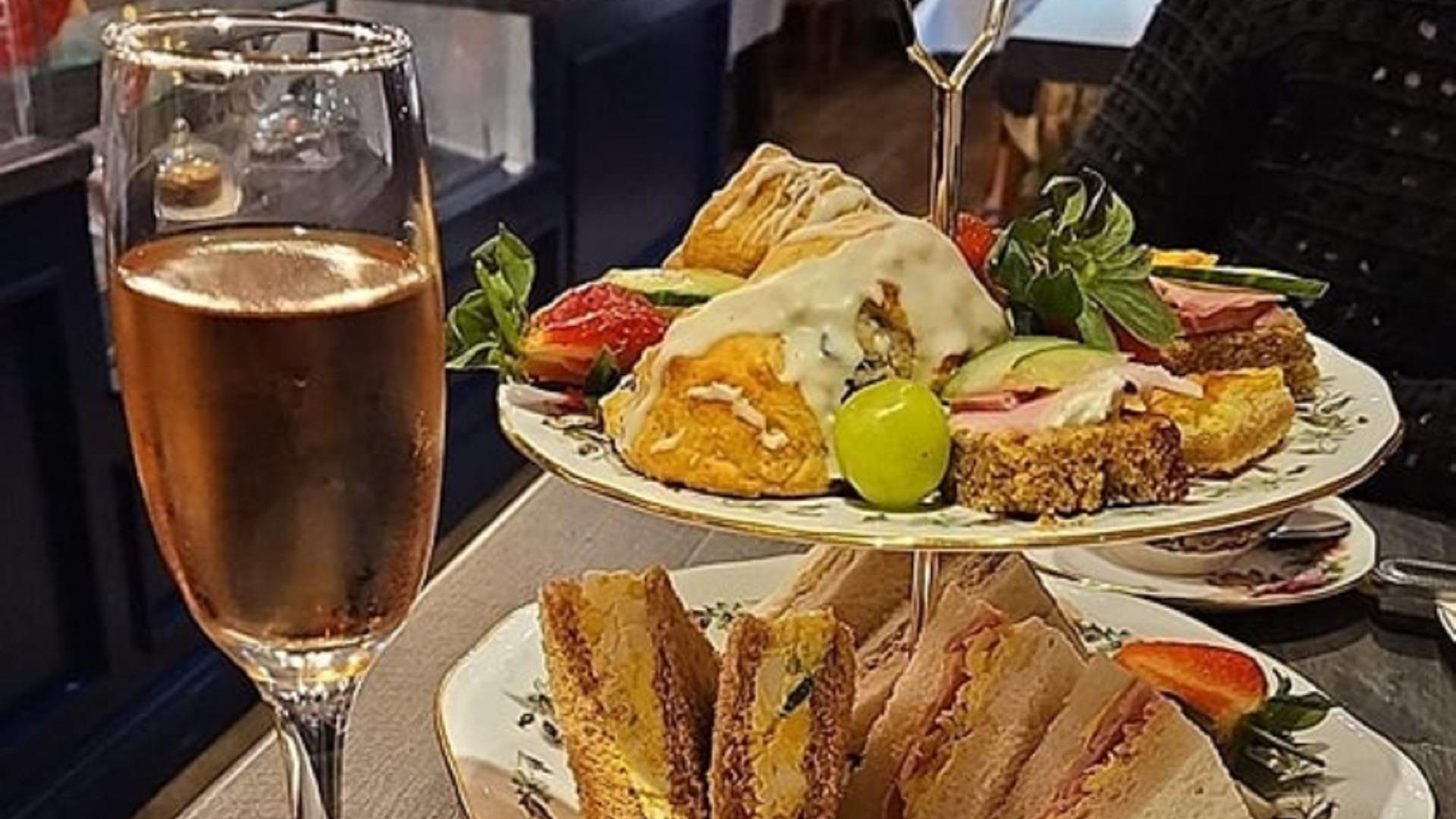 glass of prosecco next to a tiered cake stand holding sandwiches, fruit and scones