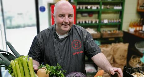 a man stands with a box filled with fresh vegetables including carrots, parsnips, celery, onions and cabbage