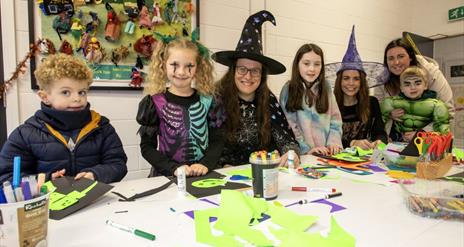 Image of children and faciltators in halloween fancy dress costumes crafting.