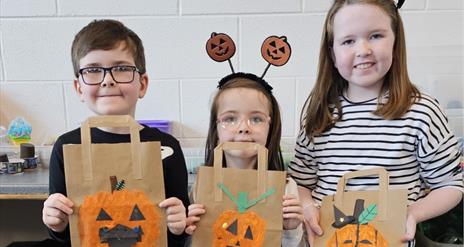 Imae of 3 children holding up their hand decorated pumpkin trick of treat bags.