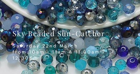 An image with many blue, turquoise and azure beads spilling out from a white porcelain bowl. White text on the front reads "Sky Beaded Sun Catcher" on