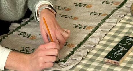 A woman carefully painting a ruffled cushion cover.