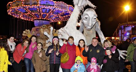 Image shows a group of people standing in front of scary Halloween characters, with a Fairground in the background