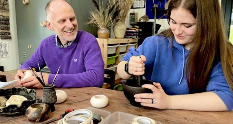 people sat at a table create designs on ceramic pots